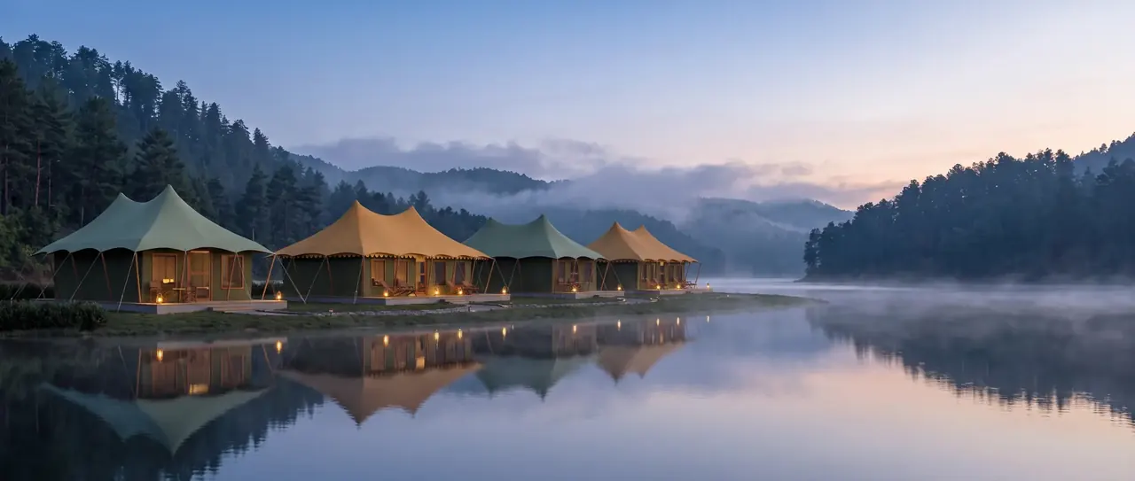 A row of twin-peaked sage and sand canvas tents with lantern-lit decks on the misty shore of a still lake at dawn, reflected in the water